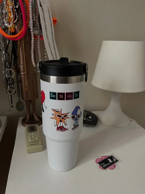 Termo blanco con stickers de personajes ilustrados y la palabra Designer en bloques de colores